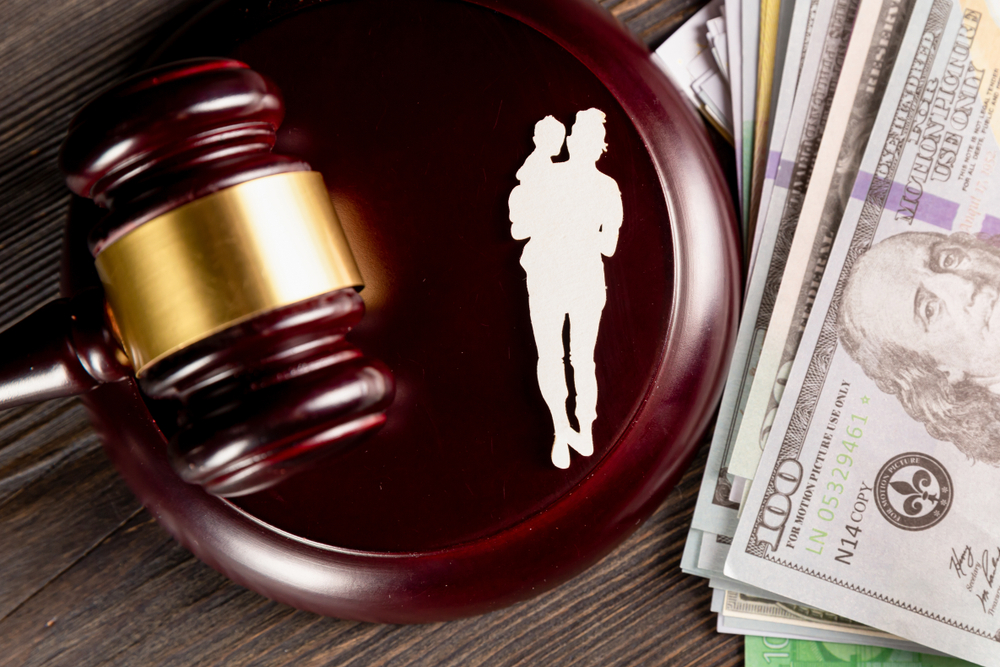 A gavel next to a cutout of a parent and child with money to the side.