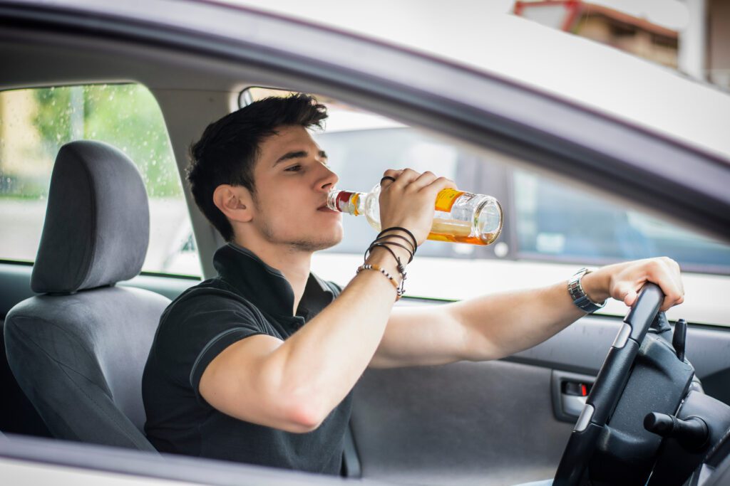 A man drinking a beer while driving a car.