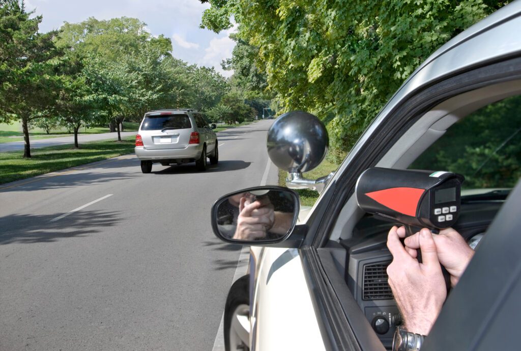 A police officer is holding a radar gun at a passing SUV.