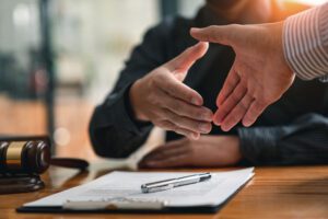 Two people finalizing a legal agreement with a handshake at a lawyer's desk.
