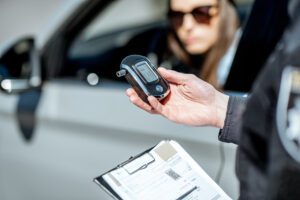 An officer administering a breathalyzer test to a woman in a car.